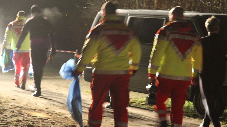 Einsatzkräfte der Polizei und Feuerwehr bringen die in blauen Tüten verpackten Leichenteile zu einem Leichenwagen.