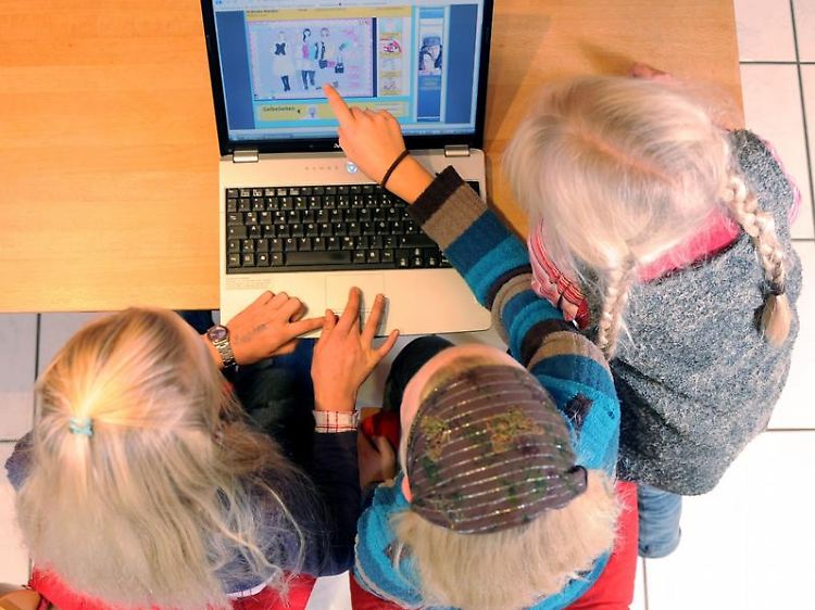 Schulkinder sitzen an einem Laptop.