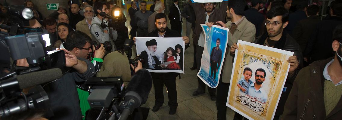 Auf dem Flughafen von Teheran demonstrieren junge Männer mit Bildern des iranischen Führers Chamenei und des Atomwissenschaftlers Mostafa Ahmadi Roshan, der am 11. Januar in Teheran bei einer Explosion getötet wurde.
