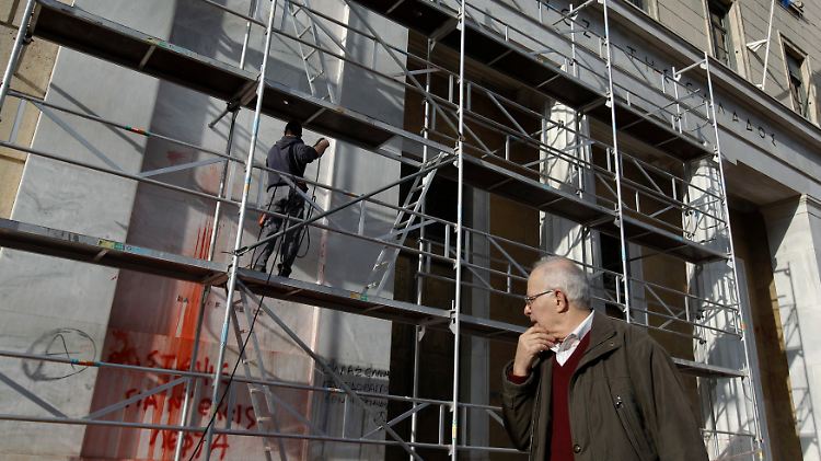 Ein Mann beobachtet, wie Schmierereien an der Fassade der griechischen Notenbank entfernt werden.