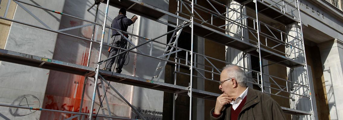 Ein Mann beobachtet, wie Schmierereien an der Fassade der griechischen Notenbank entfernt werden.