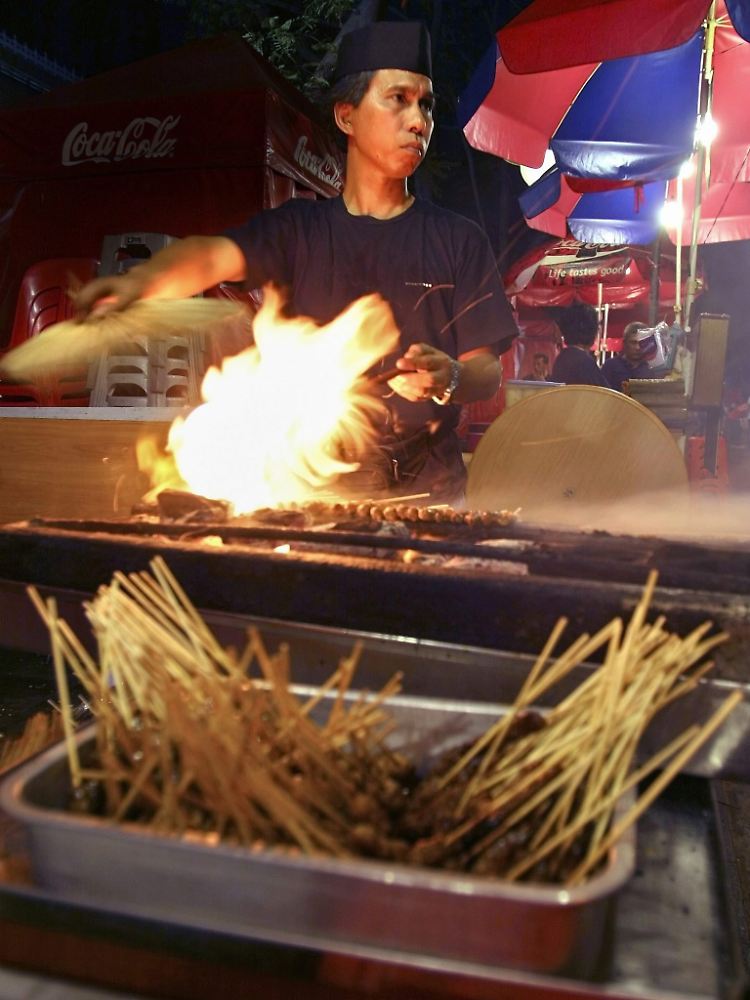 Ein Koch facht im Garküchen-Center "Lau Pa Sat" seinen Grill an.