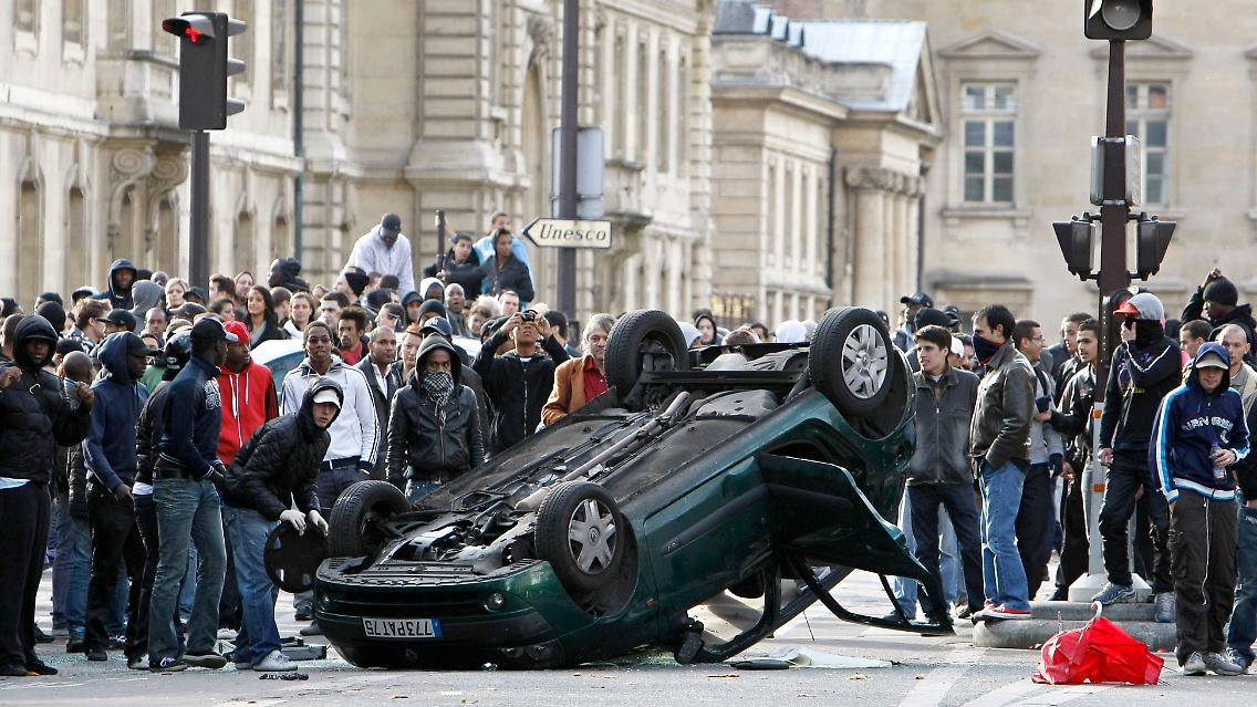 Jugendliche stehen neben dem umgestürzten Auto.