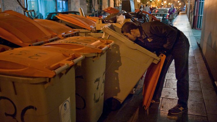 In Madrid sucht ein Mann in einer Mülltonne nach Lebensmitteln.
