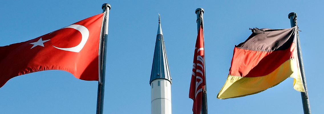 Eine deutsche und eine türkische Flagge wehen vor dem Minarett einer Moschee im Stadtteil Hassel in Gelsenkirchen.