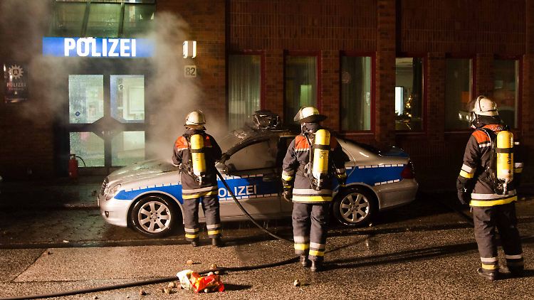 Feuerwehrleute löschen ein brennendes Polizei-Fahrzeug.