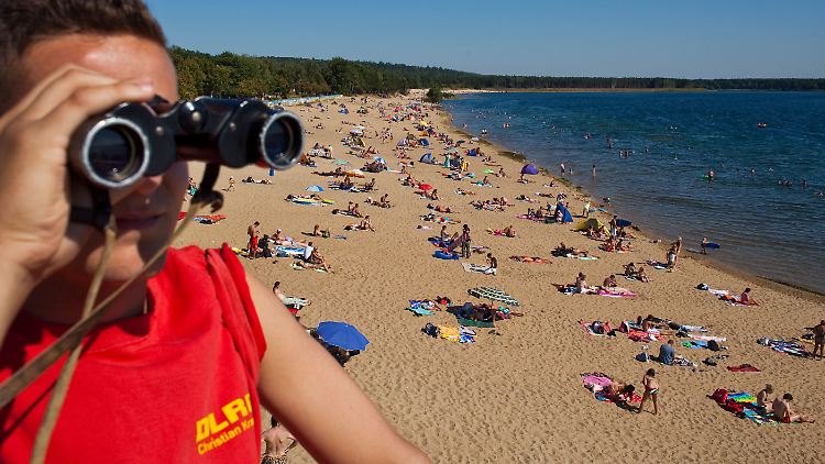 Unzählige Badegäste tummeln sich im Wasser des Helenesees, einem Tagebausee unweit von Frankfurt (Oder), während ein Rettungsschwimmer die Situation beobachtet. 