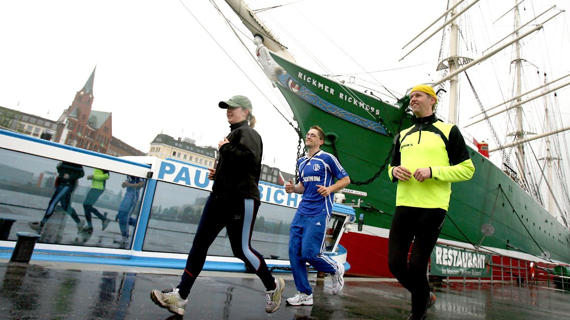 Der Stadtführer Gösta Dreise (r) und seine Gäste joggen am Schiff "Rickmer Rickmers" im Hafen von Hamburg vorbei.