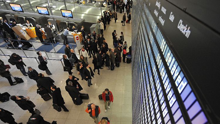 Passagier stehen am Flughafen München unter einer Anzeigetafel. Zahlreiche Flüge sind verspätet.