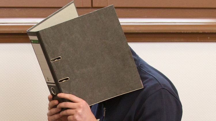 Der Angeklagte verbirgt im Gerichtssaal sein Gesicht hinter einem Aktendeckel.