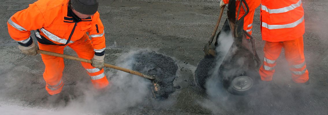 Asphaltierer reparieren notdürftig eine stark beschädigte Straße in der Südstadt von Rostock.