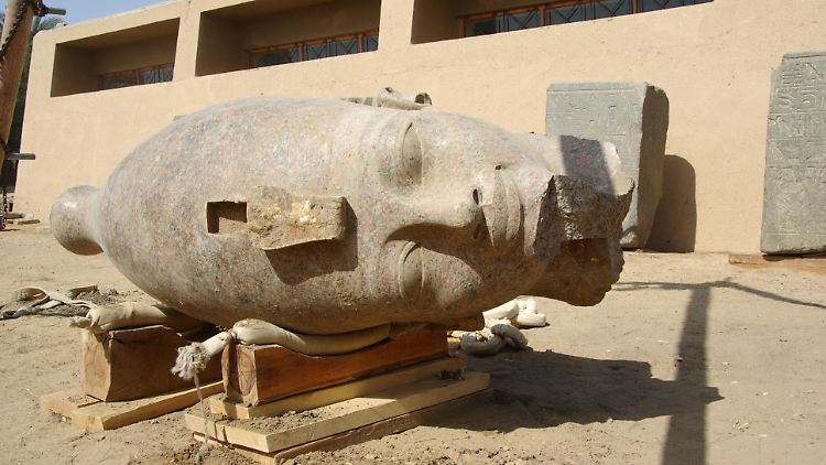 Der Kopf gehört zu einer Figur, die den Pharao sitzend mit vor der Brust verschränkten Armen zeigt.