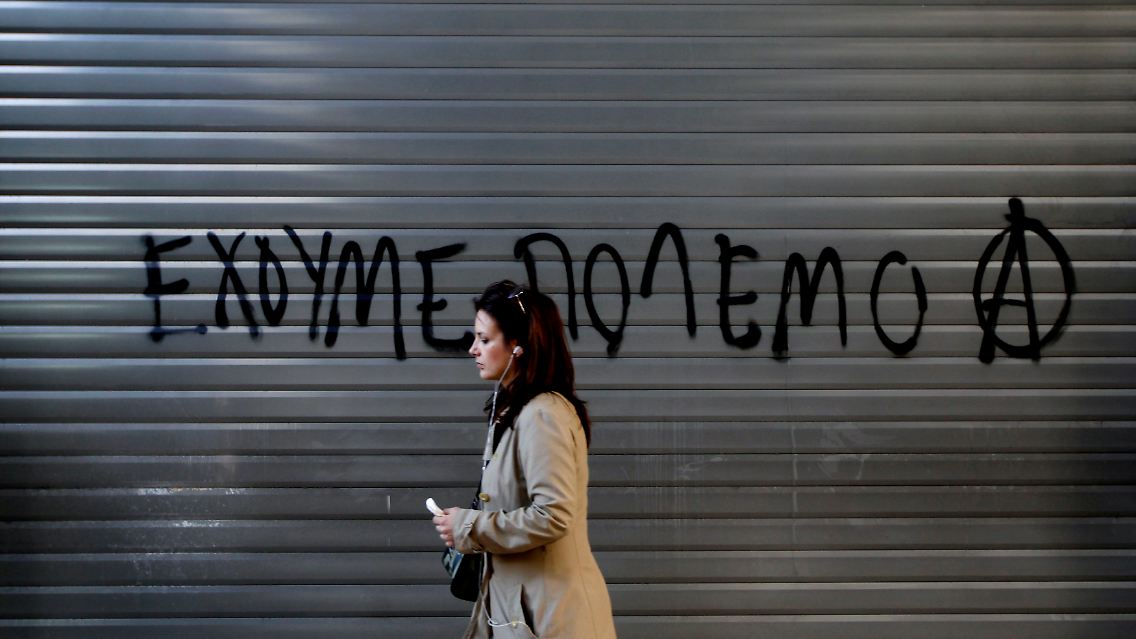 Ausnahmezustand im griechischen Staatshaushalt. Eine Frau läuft an einem geschlossenen Rollladen vorbei, auf dem Demonstranten der vergangenen Tage den Slogan "Wir sind im Krieg" aufgesprüht haben.