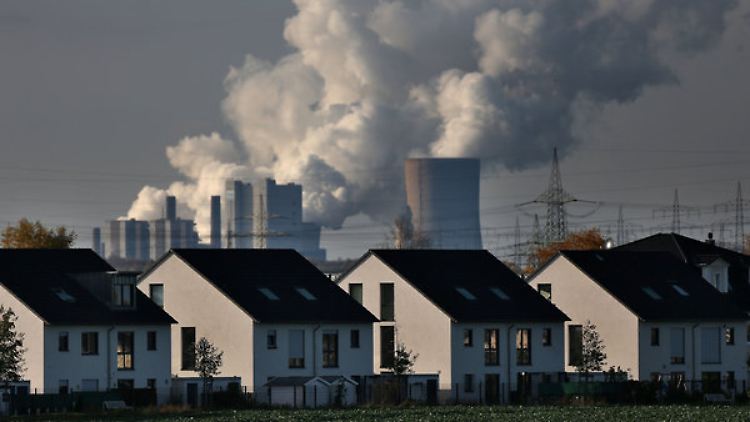 Hinter Wohnhäusern in Köln steigt Dampf aus dem RWE-Braunkohlekraftwerk Neurath auf.