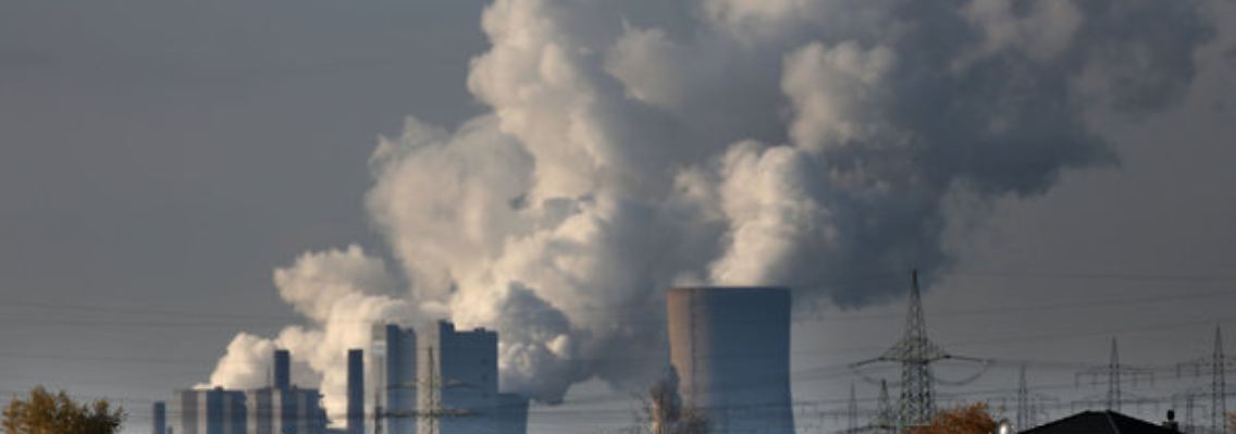 Hinter Wohnhäusern in Köln steigt Dampf aus dem RWE-Braunkohlekraftwerk Neurath auf.