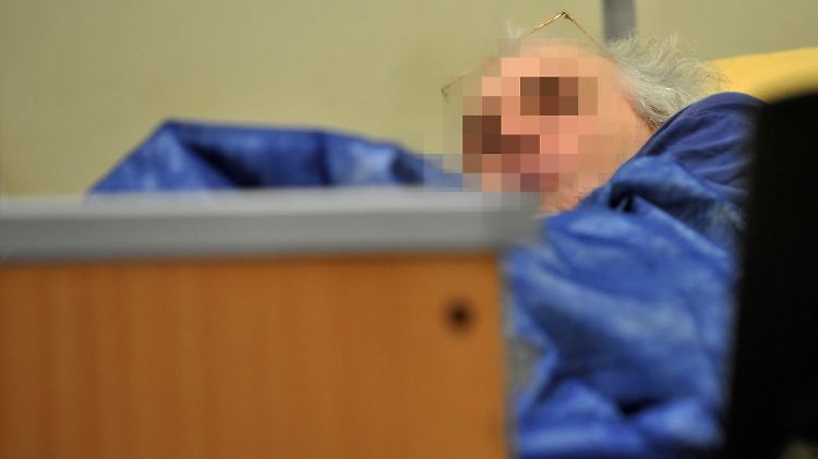 In einem Krankenbett verfolgt der Angeklagte den Prozess.