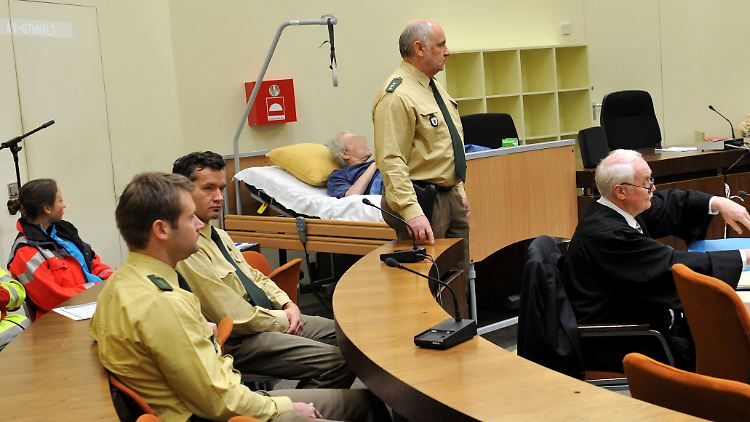 Umringt von Polizisten liegt der Angeklagte bei der Fortsetzung des Prozesses.