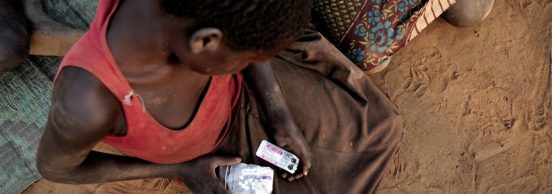 Alice Amito sitzt mit Epilepsie-Tabletten in den Händen vor einer Hütte im Kitgum Distrikt in Norduganda. Sie leidet am Kopfnicken-Syndrom.