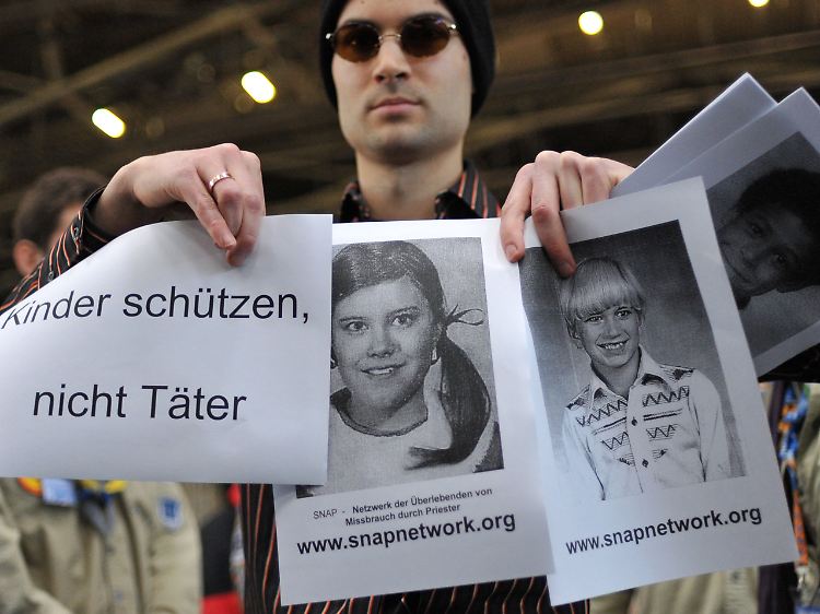 Ein Aktivist des Betroffenen-Netzwerks Snap (Survivors Network of those Abused by Priests) hält während einer Podiums-Veranstaltung zum Thema Missbrauch in der Kirche Bilder von Betroffenen hoch.