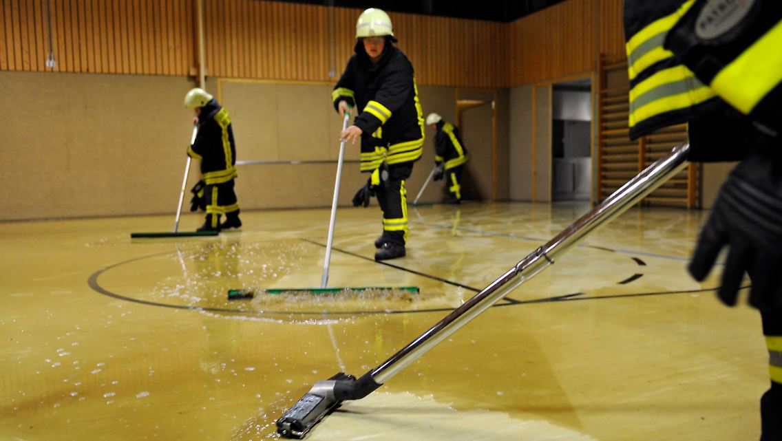Die Feuerwehr musste auch ungewohnte Aufgaben übernehmen. Hier wird die überschwemmte Sporthalle in Zepfenhan im Kreis Rottweil mit Hilfe von Schiebern und einem Wassersauger getrocknet.