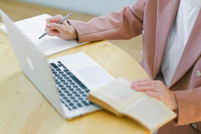 Eine Frau sitzt an einem Schreibtisch mit einem Laptop und macht etwas.