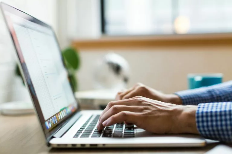 Blick von der Seite auf einen aufgeklappten Laptop auf dem eine Person etwas tippt. In unserer Schritt für Schritt Anleitung erfährst du, wie du eine Ferienwohnung Website erstellen kannst.