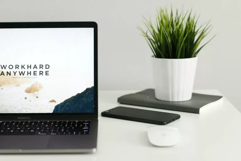Blick auf einen aufgeklappten Laptop auf einem weiÃÂen Tisch. Daneben liegt eine Computermaus und zwei Notizbücher. Wir geben dir Tipps für deine eigene Portfolio Website!