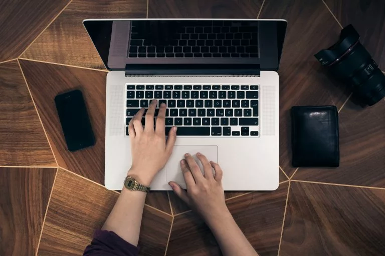 Blick von oben auf einen Schreibtisch auf dem ein aufgeklappter Laptop steht an dem eine Person arbeitet. Wir geben dir Tipps, worauf es beim Website Baukasten Vergleich ankommt!