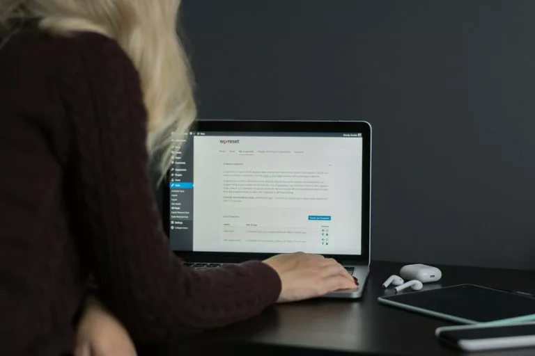 Blick von hinten ÃÂ¼ber die Schulter einer Frau, die an einem schwarzen Schreibtisch vor einer schwarzen Wand sitzt und an einem Laptop arbeitet. Wenn du einen Blog erstellen willst, geht fast nichts ÃÂ¼ber WordPress als CMS. Wir zeigen dir, was das System bietet und geben wertvolle Tipps!