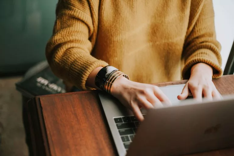 Eine Person im gelben Pulli sitzt an einem Schreibtisch und tippt auf einem Laptop. Wir zeigen dir, wie du in einfachen Schritten einen eigenen Blog erstellen kannst!