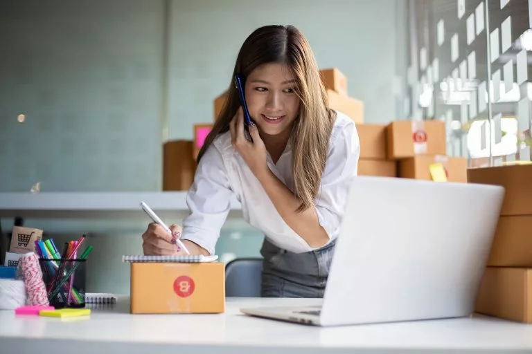Junge asiatische Unternehmerin spricht am Telefon am Arbeitsplatz zu Hause. Start up kleines Unternehmen.