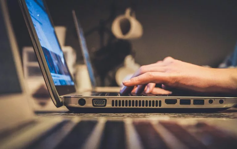 Blick von der Seite auf einen aufgeklappten Laptop an dem eine Person etwas schreibt. Wir zeigen dir, wie du Schritt für Schritt einen Onlineshop erstellen kannst!