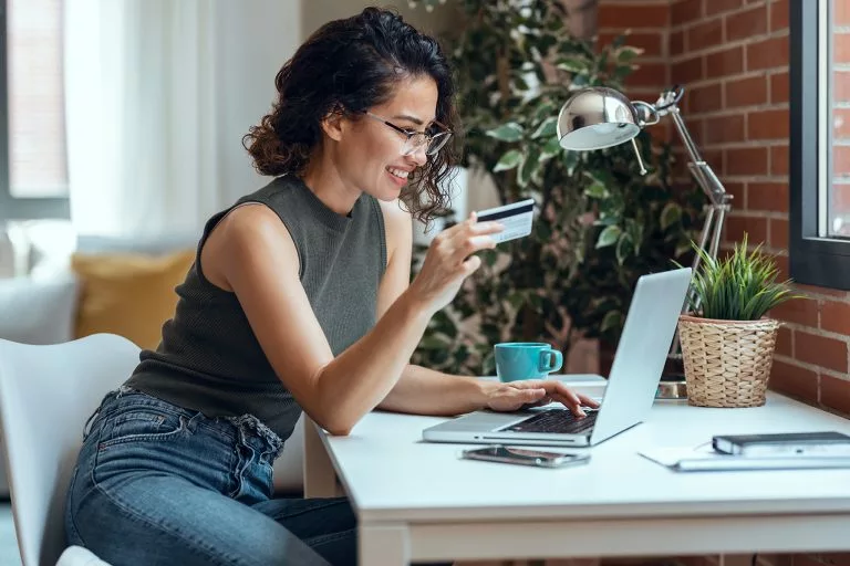Shot of cute woman holding white credit card for shopping online with computer while sitting in living room at home.Shot of cute woman holding white credit card for shopping online with computer while sitting in living room at home.Cute woman holding white credit card for shopping online with co