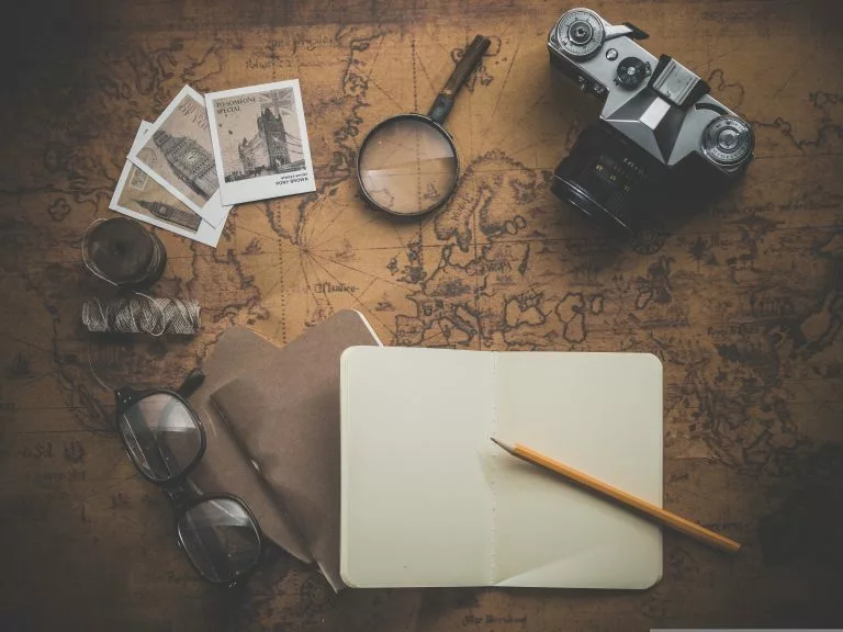 Auf einer alten Landkarte sind ein Fotoapparat, eine Lupe, Bilder, eine Lesebrille, ein Papier und ein Stift angebracht.