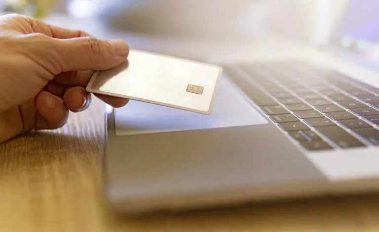 eine Hand hÃ¤lt eine Kreditkarte neben einem Laptop, der das Online-Shopping symbolisiert.